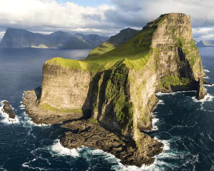 Grüne Klippen umgeben von Wasser und Bergen im Hintergrund